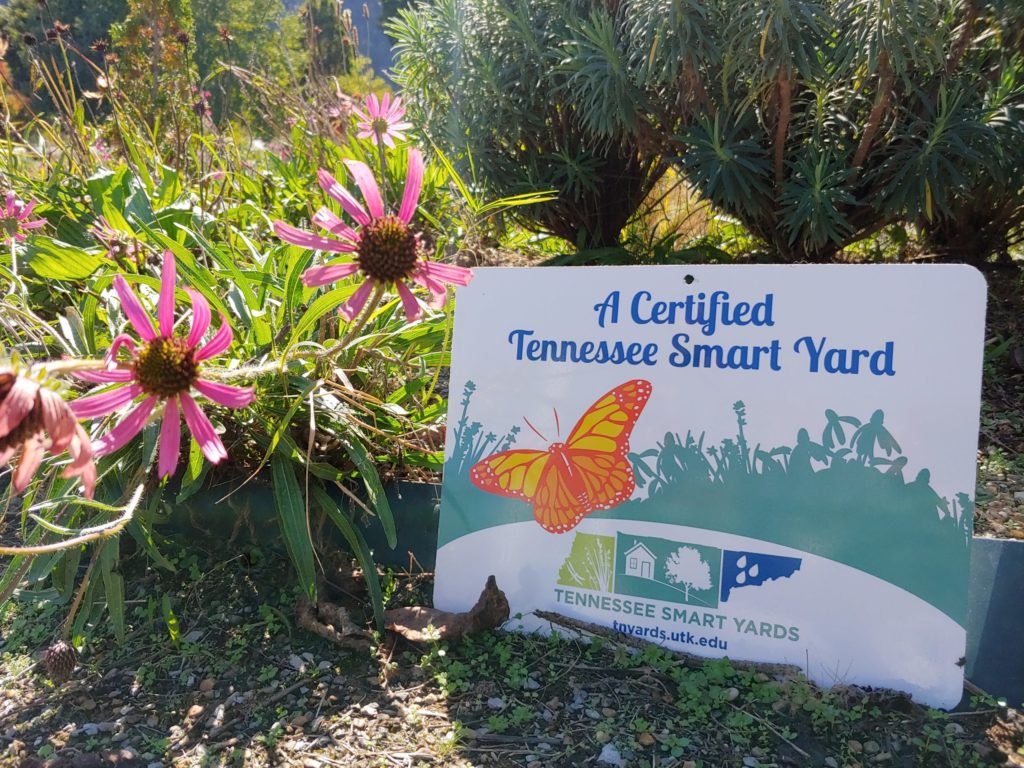 A Tennessee Smart Yard Certification Sign on the ground near pink flowers.