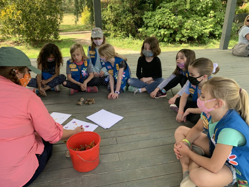 Girl Scouts and instructor sitting in a circle on a stage.