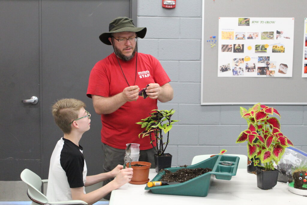 Image of adult man showing a boy a plant as they work on the planting project together.