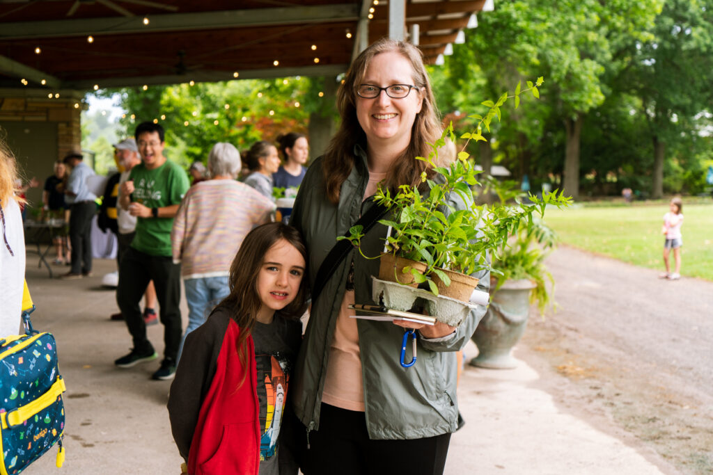 A child and a woman pose while holding a plant