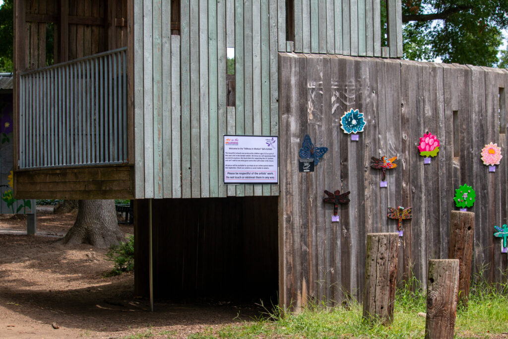 Wooden wall featuring wooden kids' art pieces from Art in the Garden 2024 (Stillness in Motion: A Dragonfly Exhibit)