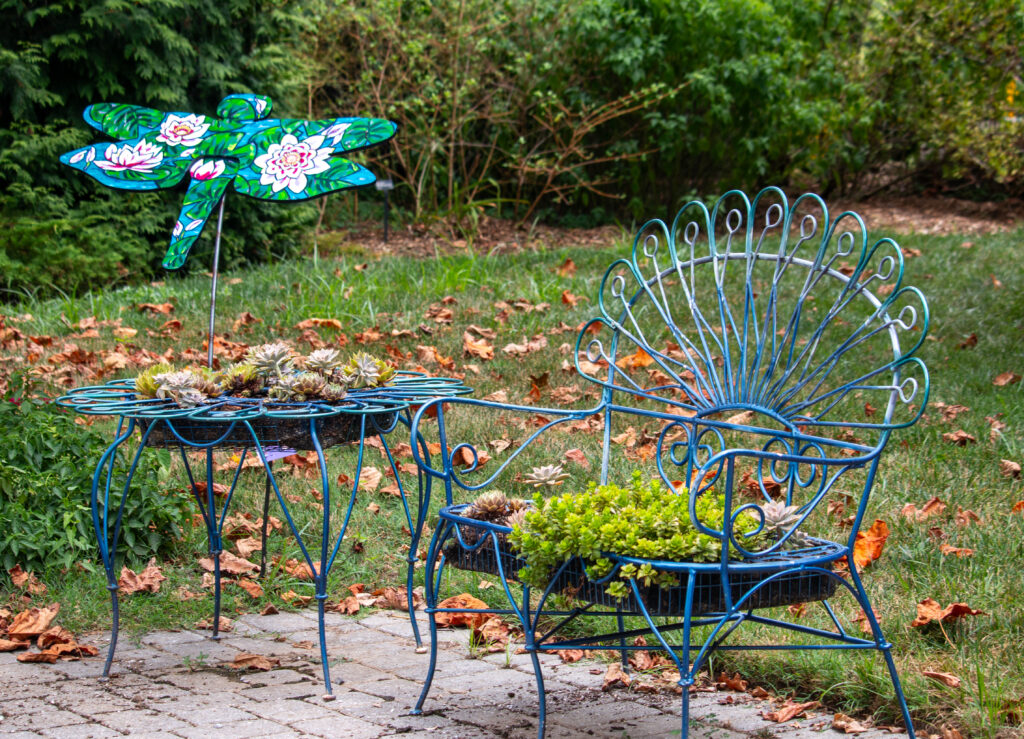 A blue metal patio bench and table that are being used as containers for succulent plantings at the edge of the plaza