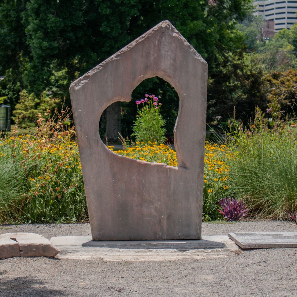 A carved heart statue overlooking some pollinator plants