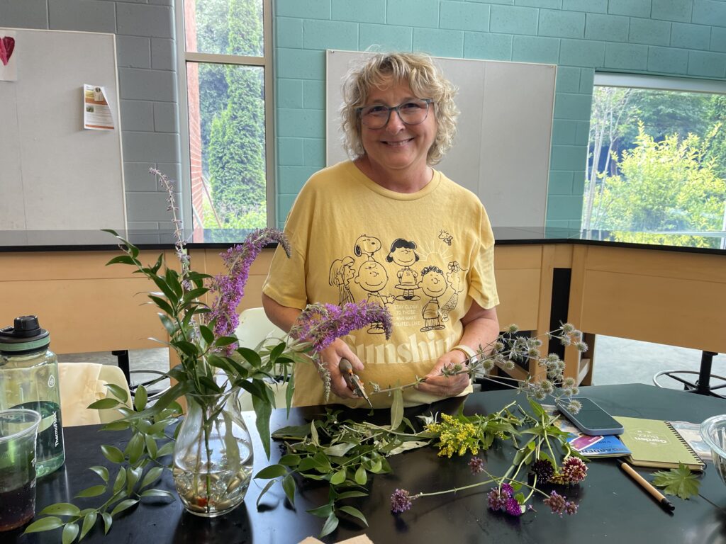 Woman indoors at a table of plants being used in a floral arrangement