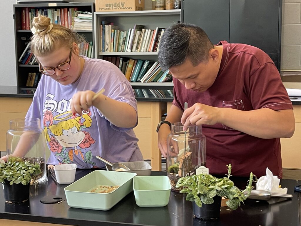 A woman and a man adding items to glass terrarium jars