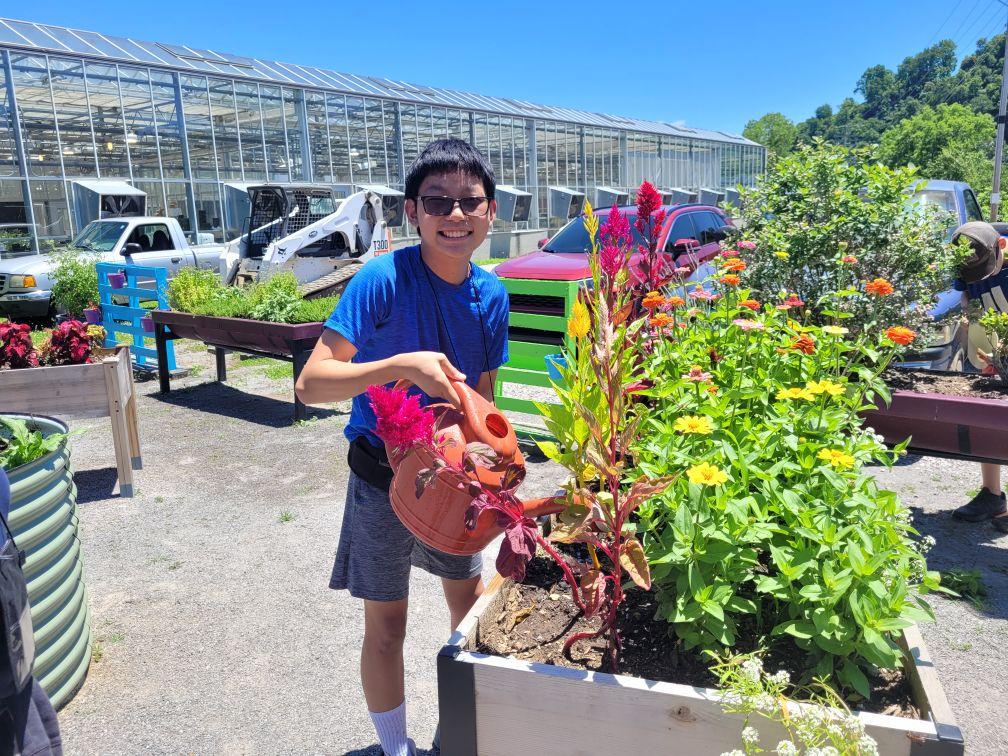 Smiling teen watering plants with a watering can outside