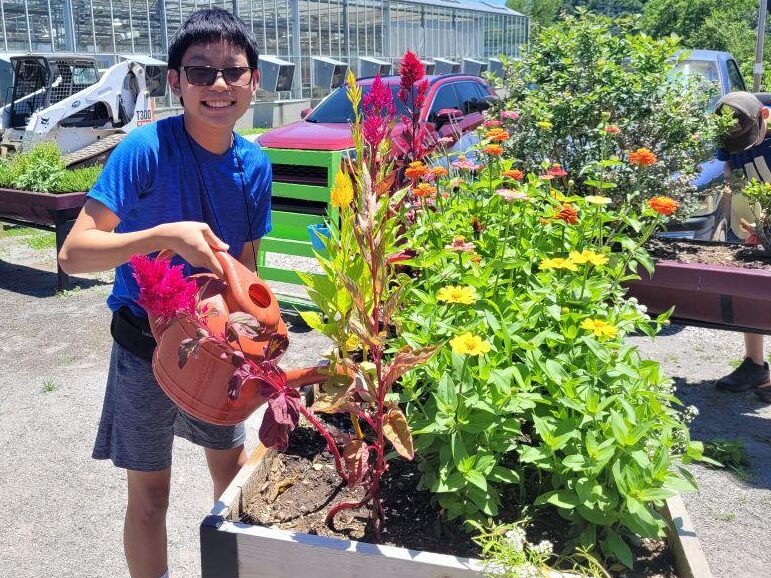 Smiling teen watering plants with a watering can outside