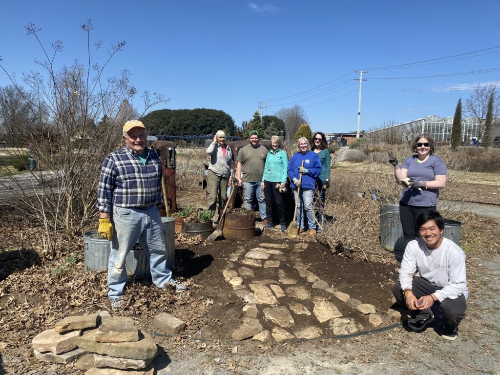 a group of volunteers stands around the hardscapes they just installed to create a new path in the gardens